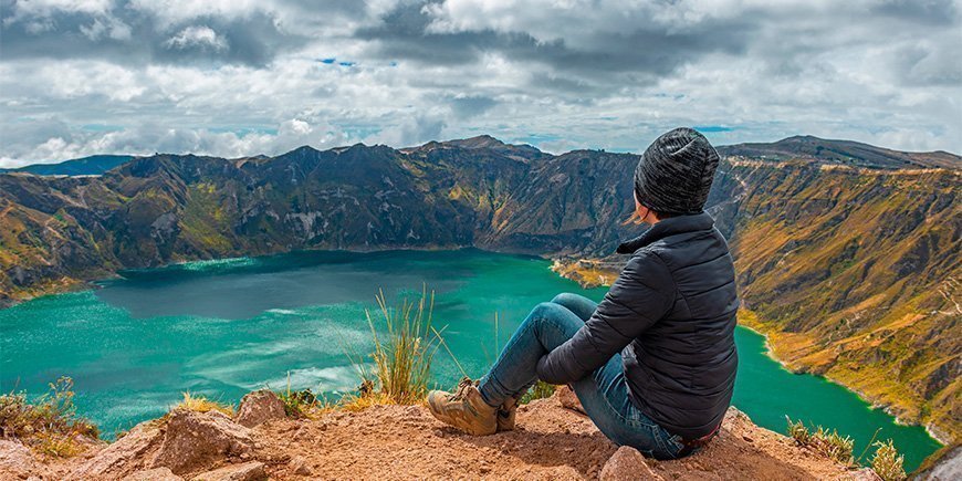 Kvinne sitter på kanten av kratersjøen Quilotoa i Ecuador.