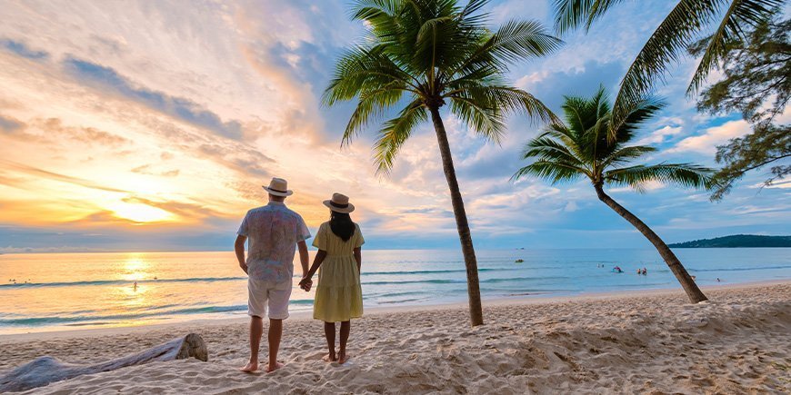 Et par holder hverandre i hånden og ser på solnedgangen på stranden i Phuket